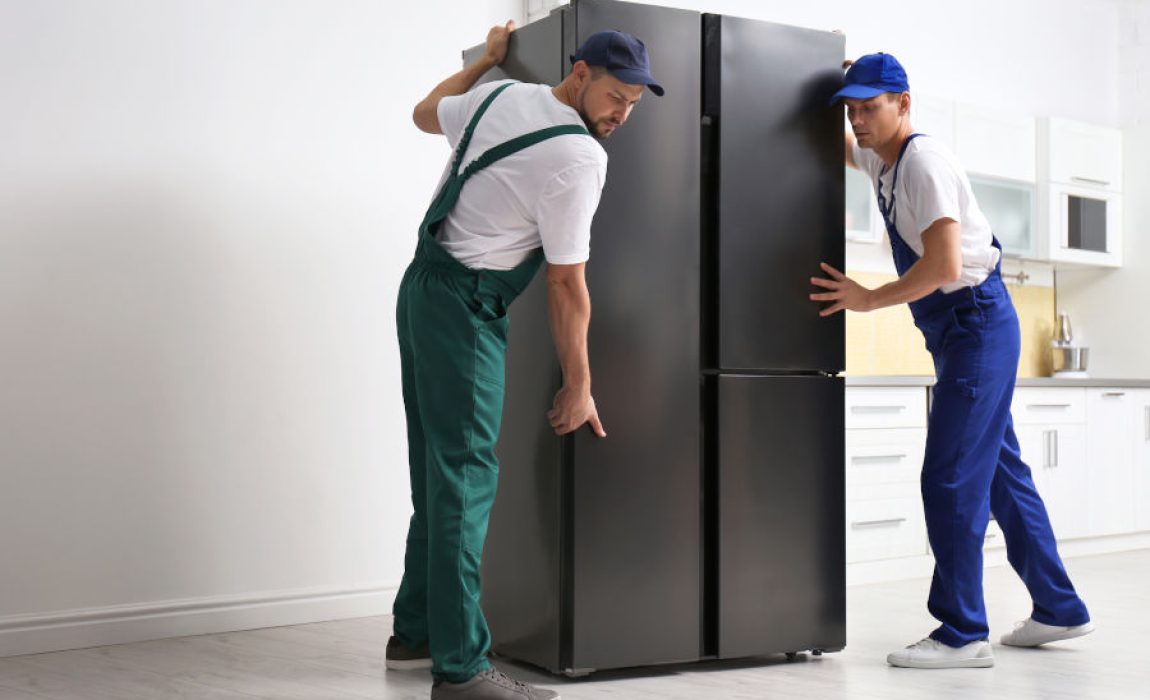 Professional workers carrying modern refrigerator in kitchen